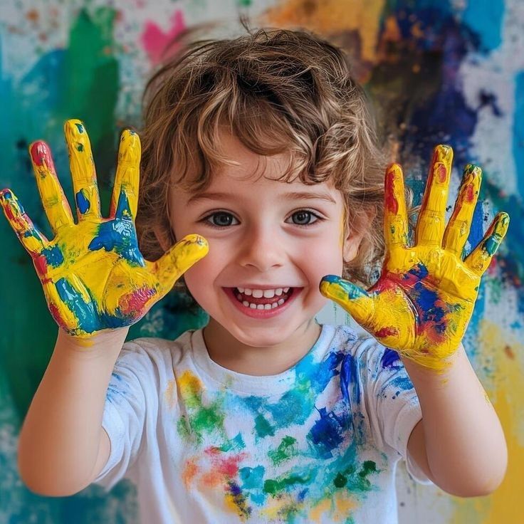 Smiling child with curly showing colorful painted hands,wearing a paint-stained shirt,in a playful art setting