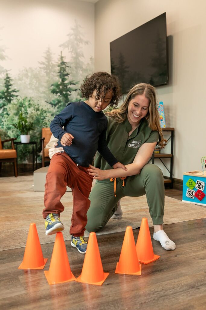 Child walking throughb orange cones with therapists help