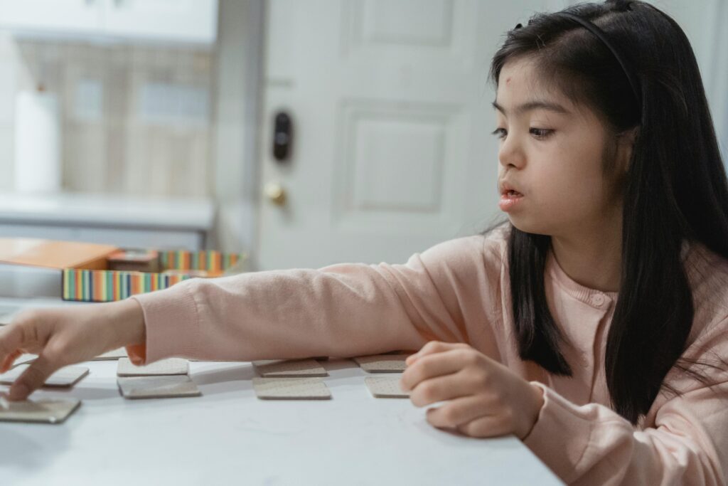 Young Asian girl with Down Syndrome engaged in a game indoors, wearing a pink sweater.